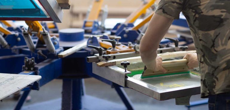 Worker and Serigraphy silk screen print process at clothes factory.