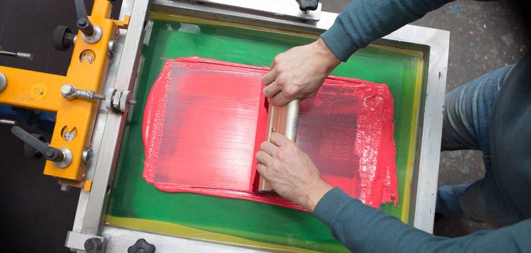 Silk screen printing. Serigraphy. Color paints and fabric. Plastisol paint and squeegee.